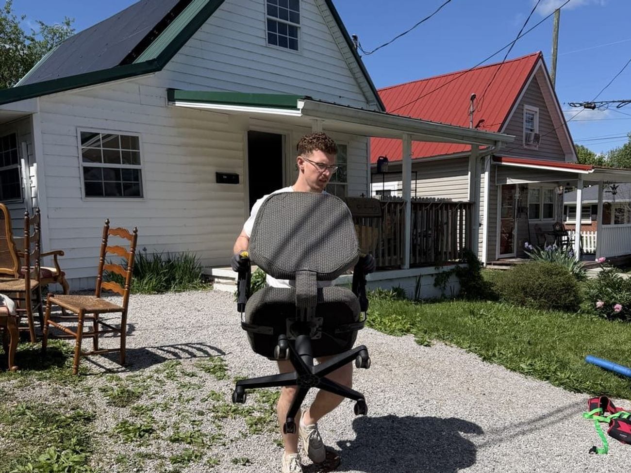 A crew member carrying an office chair across the yard out to the truck.