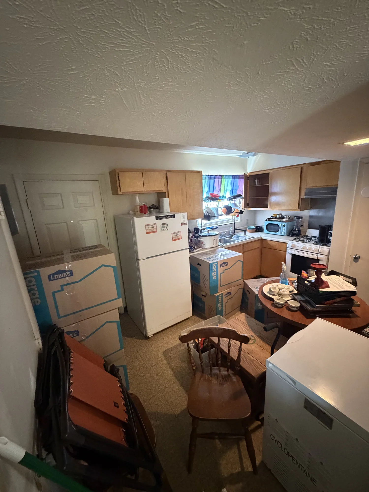 Housing Authority apartment kitchen before cleanout, packed with stacked moving boxes, folded chairs and dishes on the table.