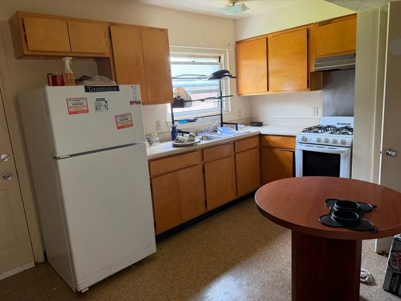 The same kitchen after cleanout, wood cabinets, sink under the window and stove with counters and floor cleared.